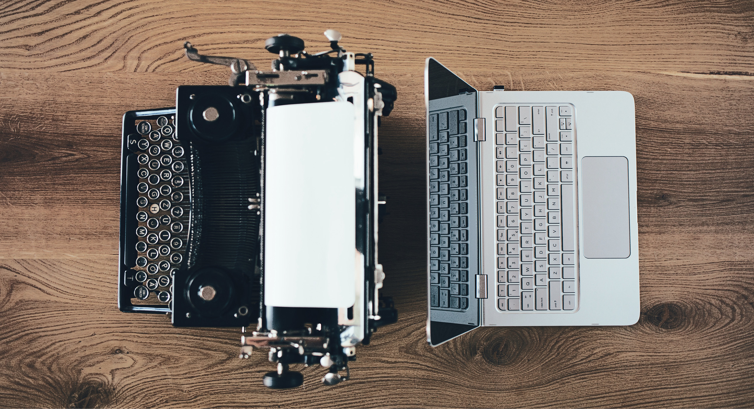 A typewriter and laptop on a wooden table.