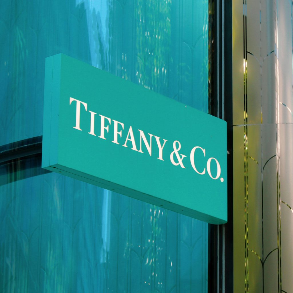 Tiffany & Co. storefront sign in robin's egg blue mounted on a reflective teal glass facade.