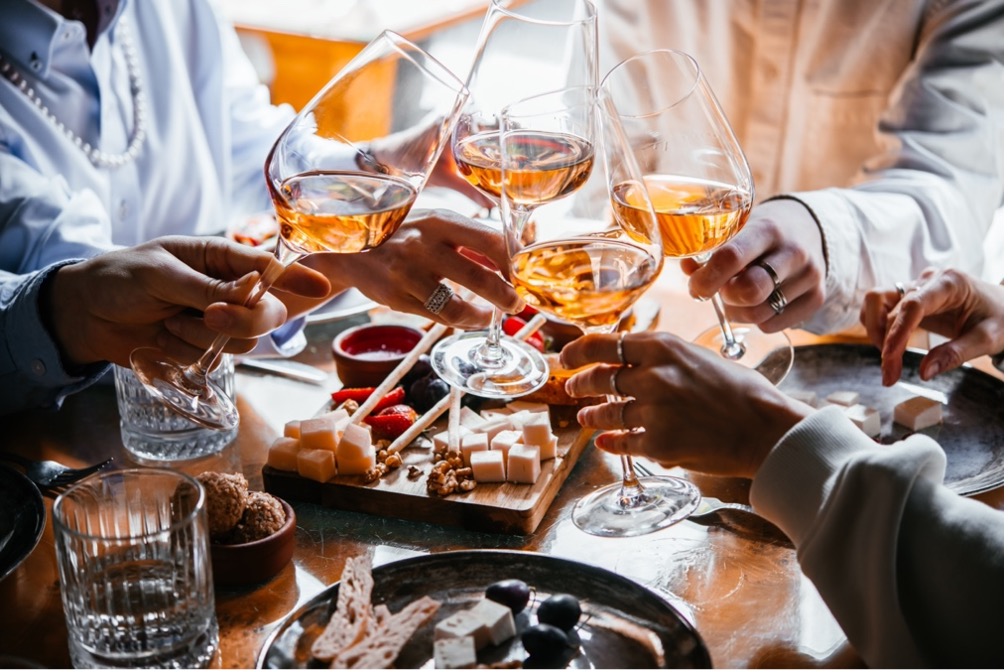 Guests toasting with rosé wine over a charcuterie board at a hotel bar.